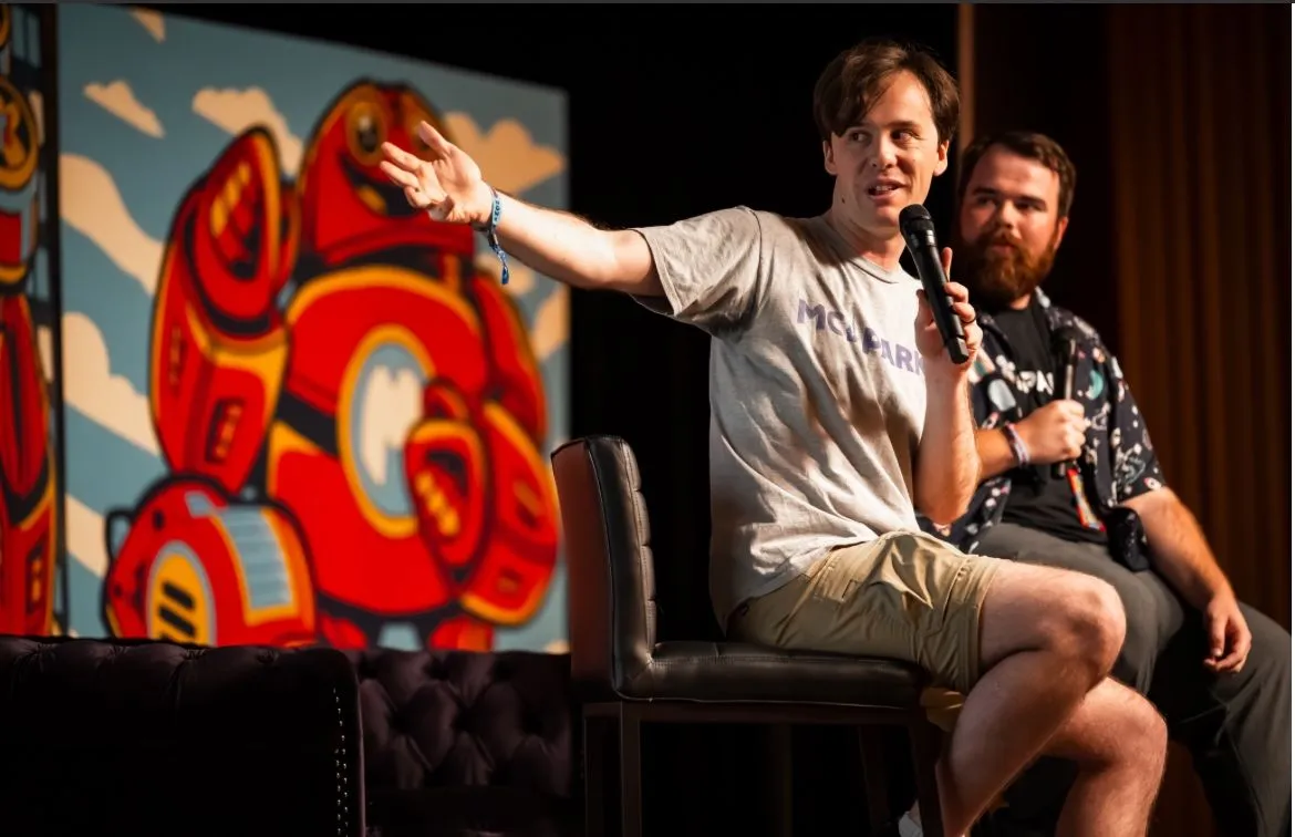 Ryan Hecht speaking into a microphone on the Maker Faire Orlando main stage while fellow MCParks Owner Darren sits beside him