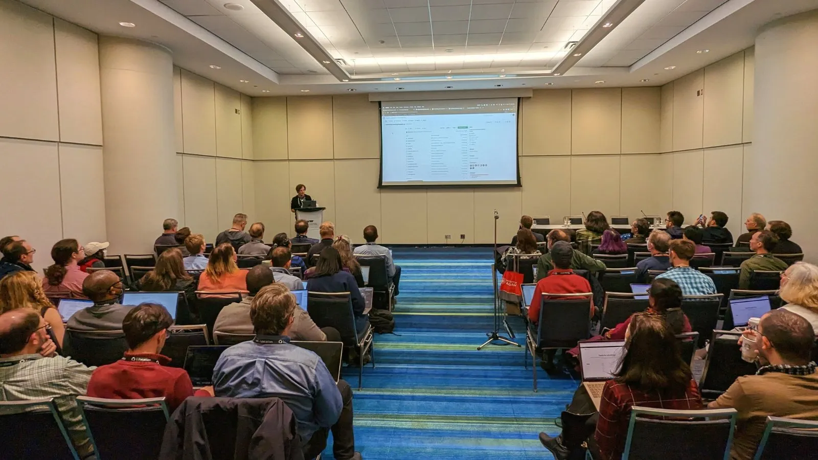 Ryan presenting to a seated audience at SIGCSE TS 2023 with GitHub Classroom projected behind him